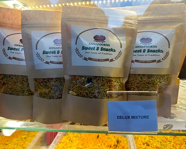 Annapoorna Sweet & Snacks pouches above a tray labelled Delux Mixture at the shop counter