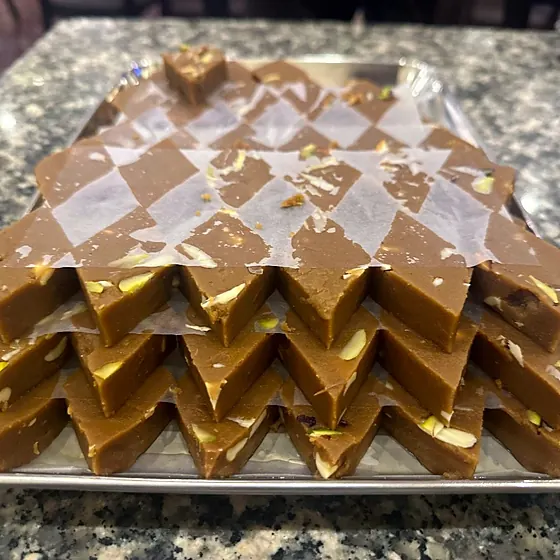 Kaju Anjeer Burfi — layered fudge pieces with pistachio on a shop tray
